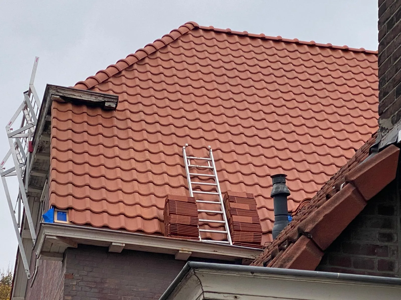 Rood pannendak tijdens werkzaamheden, met dakpannen, nok en dakdoorvoer.